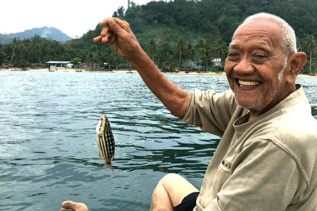Seorang kakek tersenyum saat mendapati seekor ikan dengan pancing di kawasan Teluk Buo Padang. (GATRA/Dok.KopiBatigo)